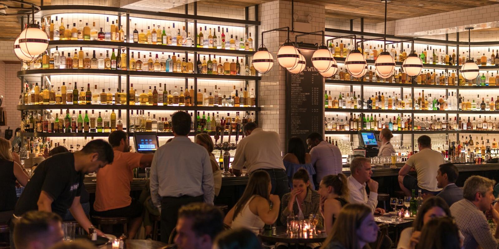 Experience the lively atmosphere of a bustling New York City bar with patrons enjoying nightlife within a stylish indoor setting.