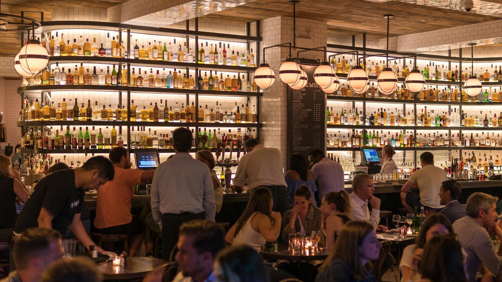 Experience the lively atmosphere of a bustling New York City bar with patrons enjoying nightlife within a stylish indoor setting.