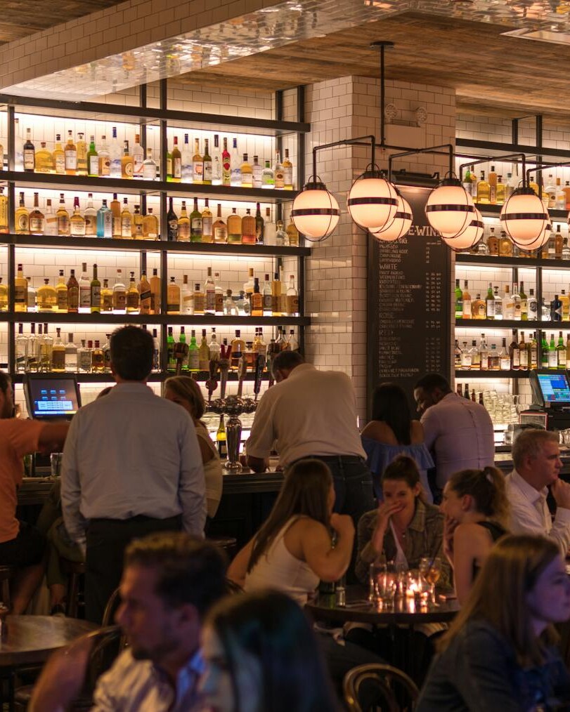 Experience the lively atmosphere of a bustling New York City bar with patrons enjoying nightlife within a stylish indoor setting.