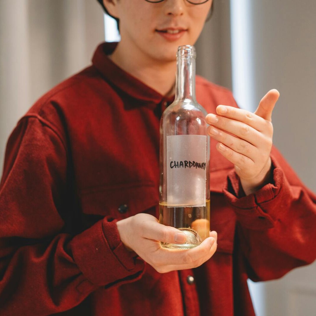 Close-up of a person in red holding a Chardonnay wine bottle indoors, highlighting wine culture.