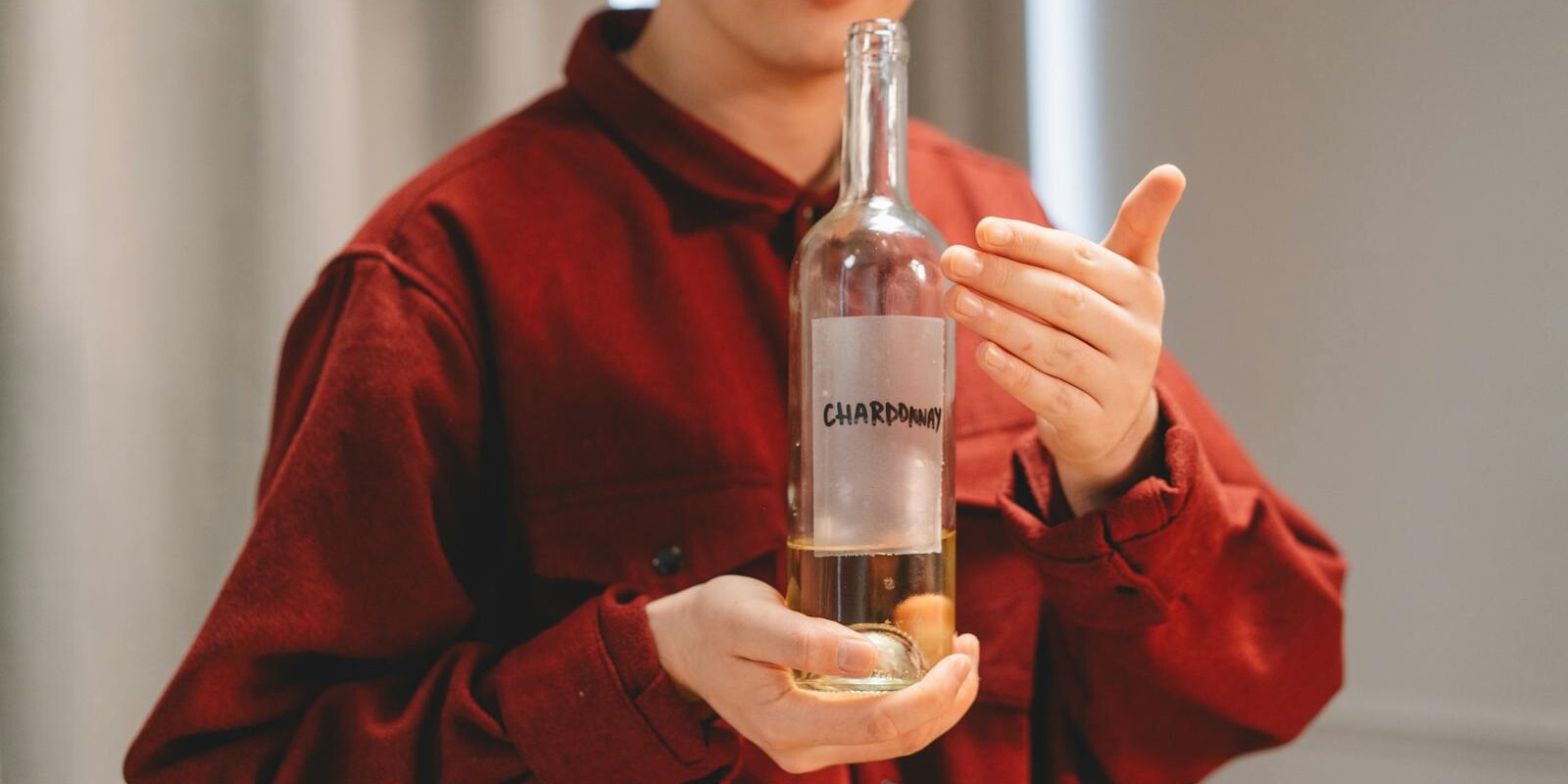 Close-up of a person in red holding a Chardonnay wine bottle indoors, highlighting wine culture.