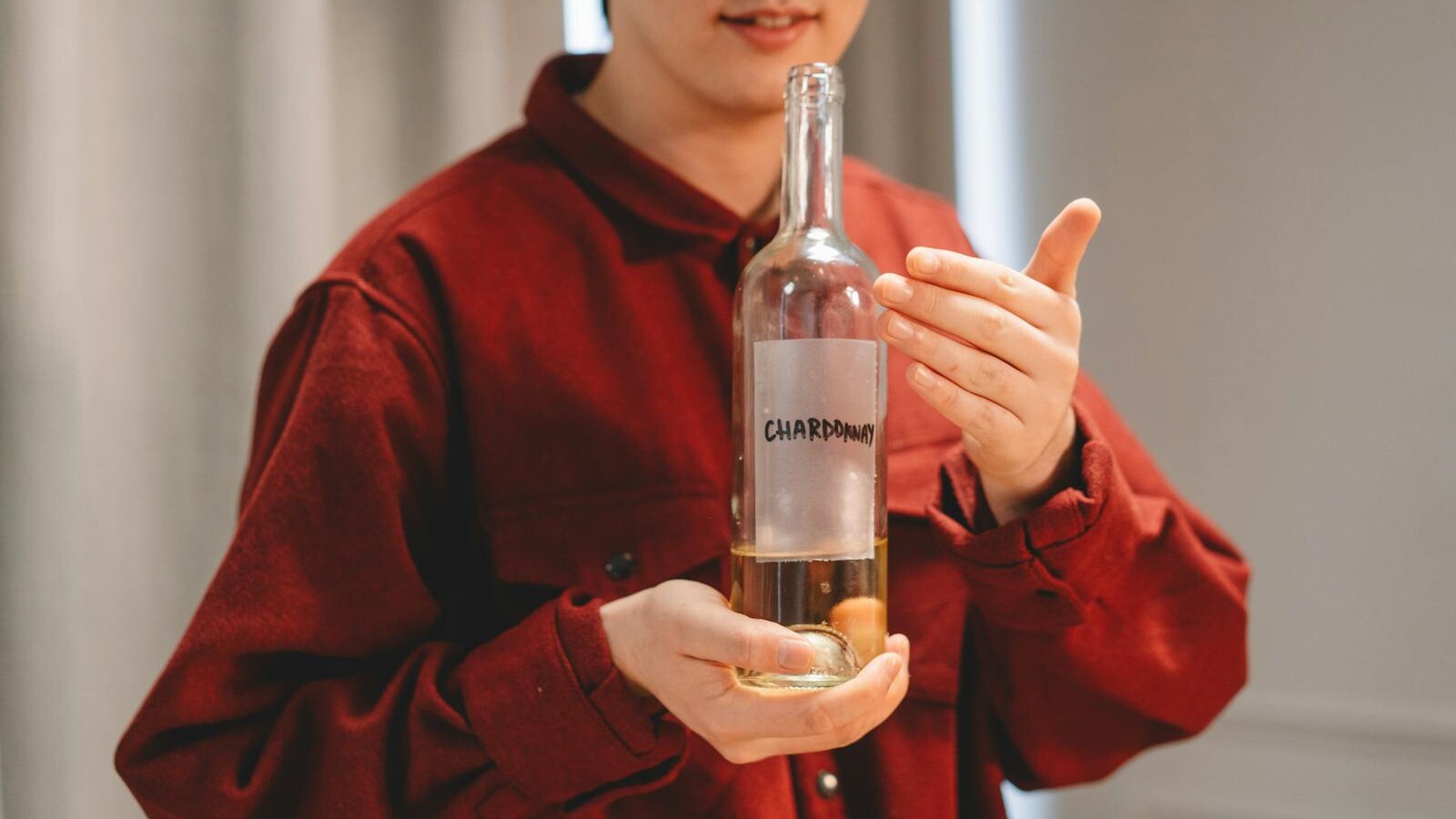Close-up of a person in red holding a Chardonnay wine bottle indoors, highlighting wine culture.