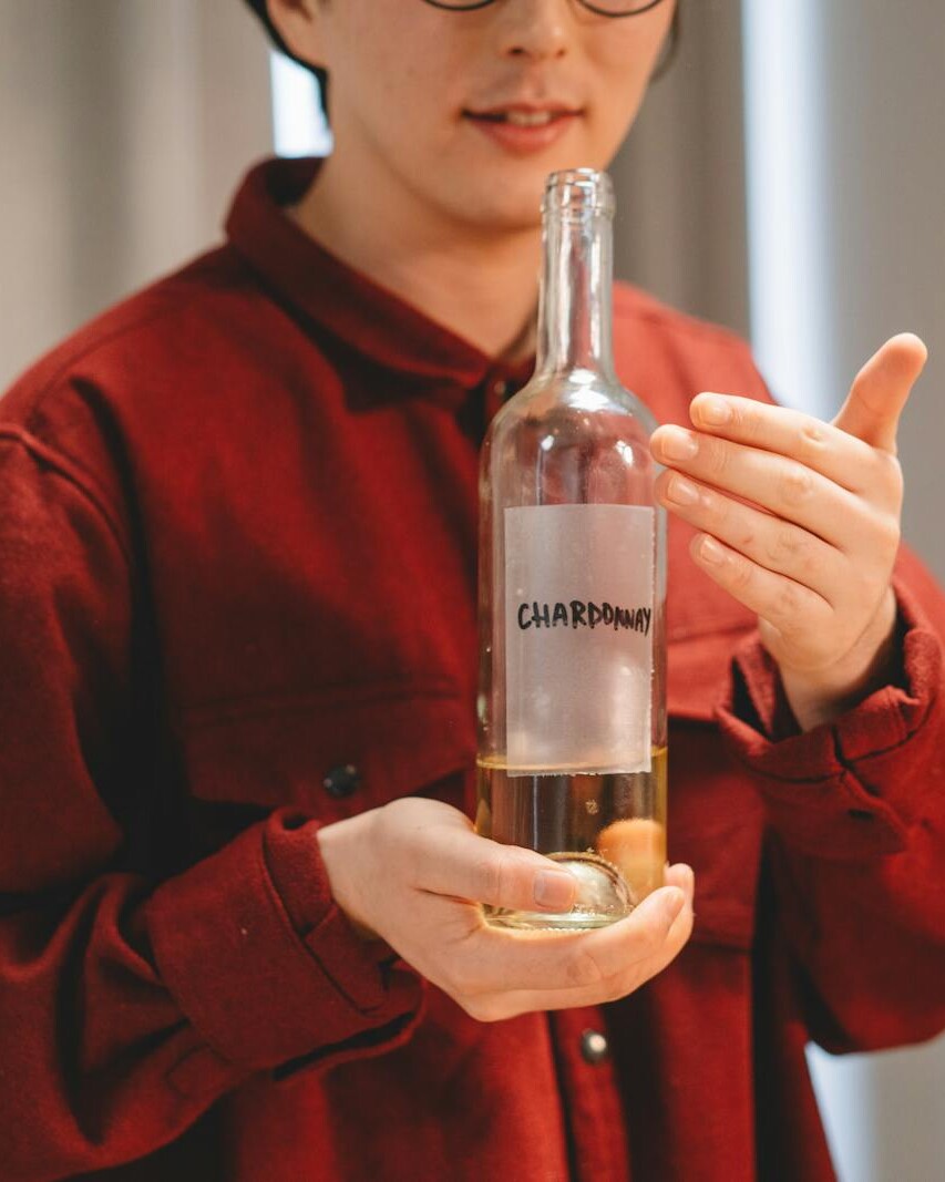 Close-up of a person in red holding a Chardonnay wine bottle indoors, highlighting wine culture.