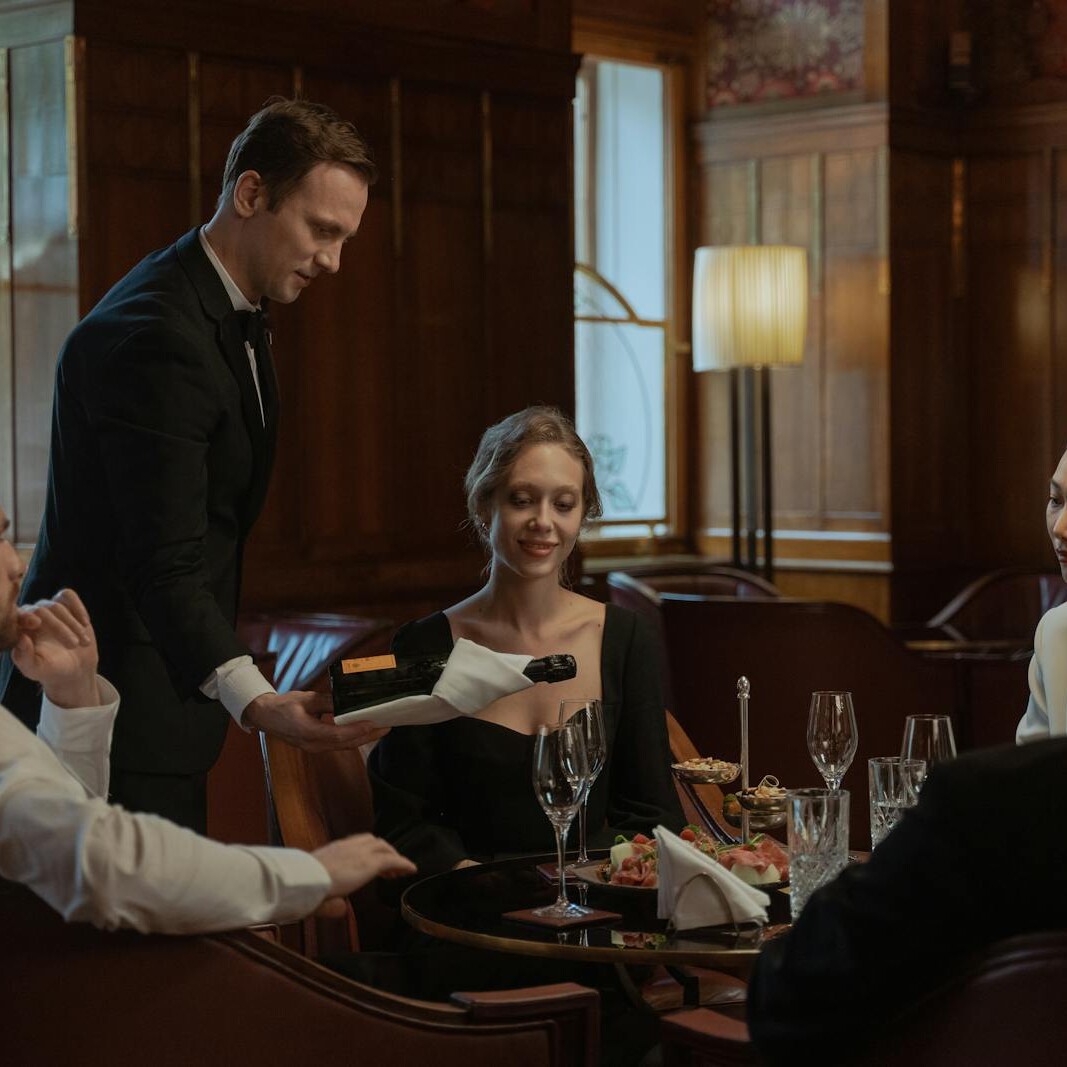 A waiter serves wine to a diverse group enjoying an elegant meal indoors.
