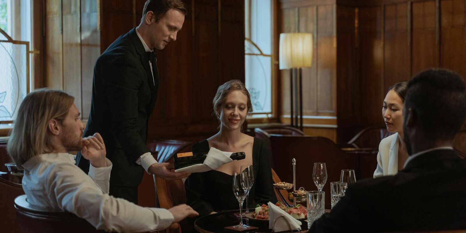 A waiter serves wine to a diverse group enjoying an elegant meal indoors.