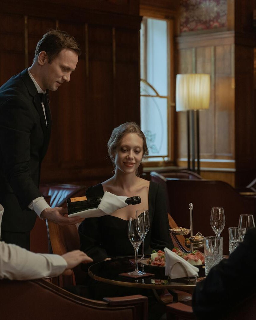 A waiter serves wine to a diverse group enjoying an elegant meal indoors.