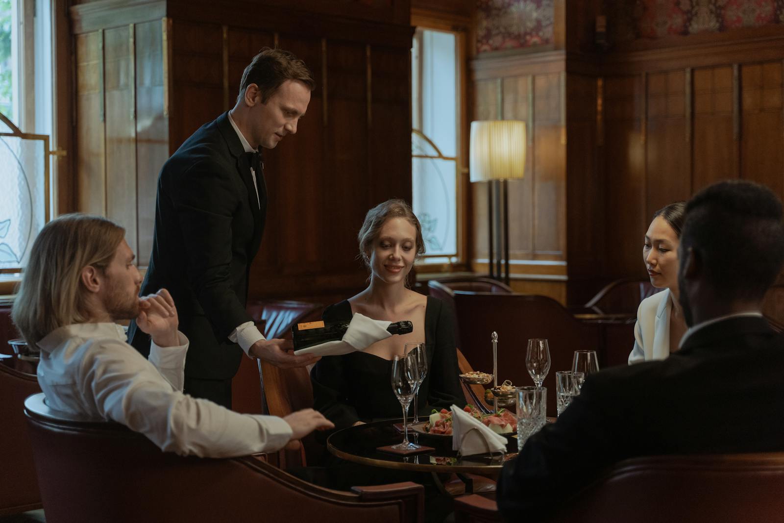 A waiter serves wine to a diverse group enjoying an elegant meal indoors.