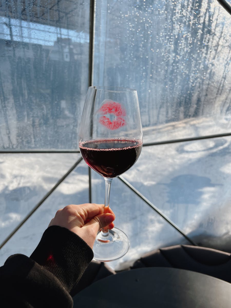 Hand holding a red wine glass with a lipstick mark against a snowy backdrop.